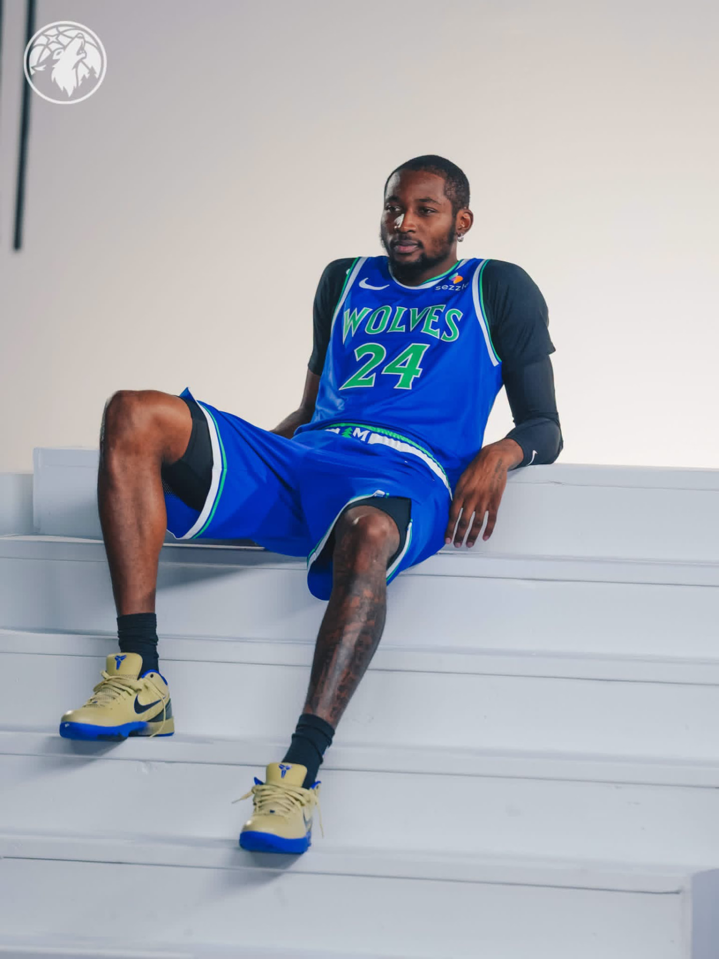 Jonathan Kuminga leaning back on white steps in the blue Wolves #24 uniform